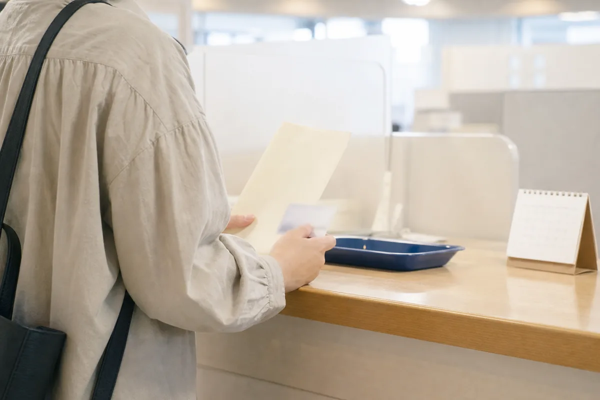市区町村の窓口を想定した場所で、封筒とカードを手に手続きの準備をする様子