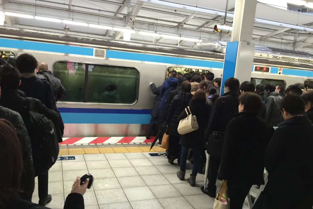 朝の浦安駅のホームで列をつくって電車を待つ通勤客