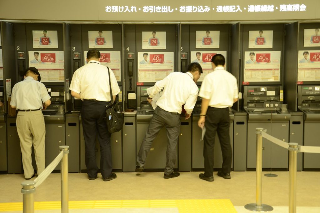東京・汐留のATMコーナーで機械を操作する会社員たちの後ろ姿